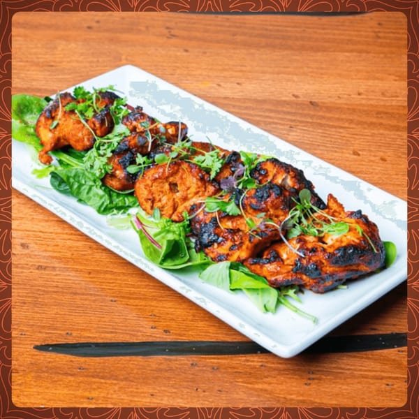 Spice Social's Indian grilled chicken pieces, garnished with fresh herbs, served on a bed of greens.