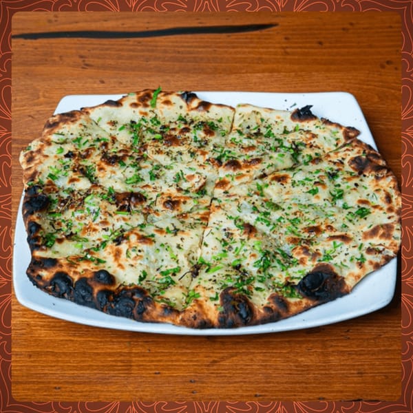 Garlic naan bread, garnished with fresh herbs, sliced and served on a white plate at Spice Social.