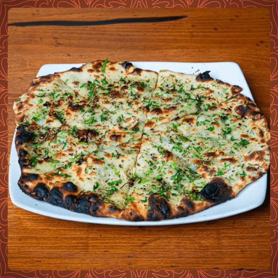 Garlic naan bread, garnished with fresh herbs, sliced and served on a white plate at Spice Social.