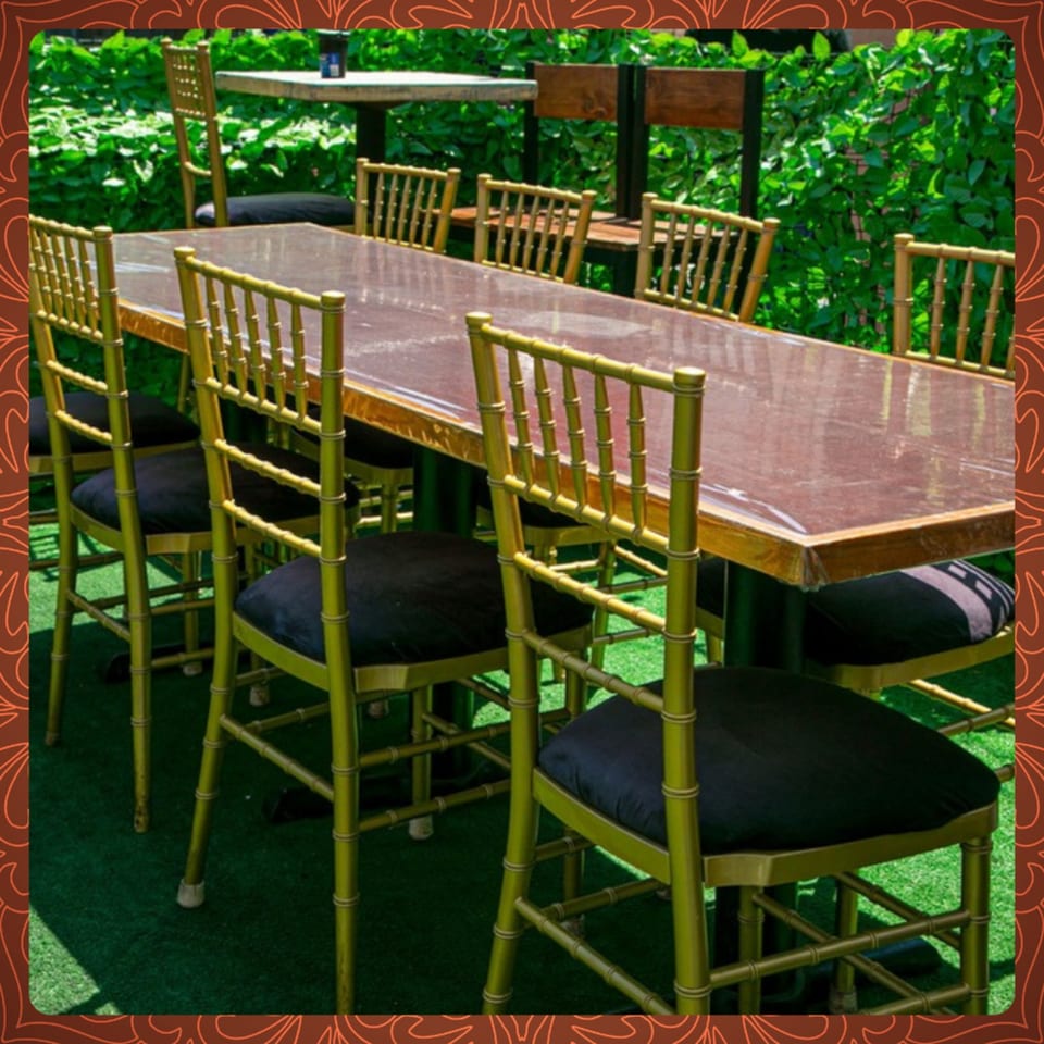 Long dining table with gold bamboo-style chairs and black cushions on a green turf patio.