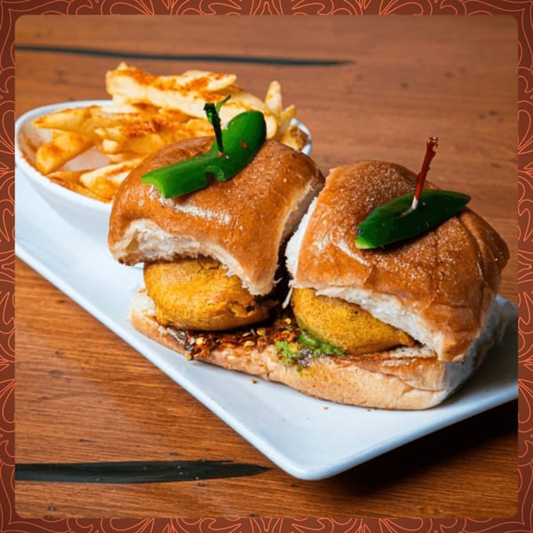 Two Indian vada pav sliders with green chili garnishes and a side of french fries.