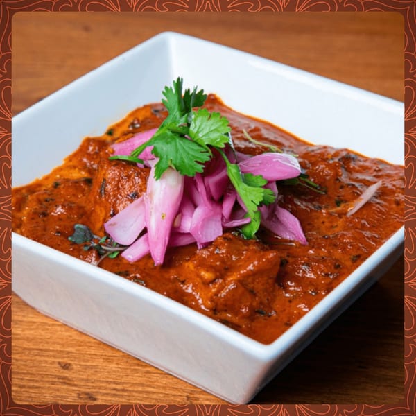 Indian butter chicken in a white bowl, garnished with cilantro and pickled red onions.