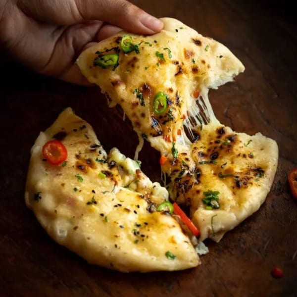 Hand pulling apart cheesy naan bread with green chilies and cilantro, showing melted cheese strings.