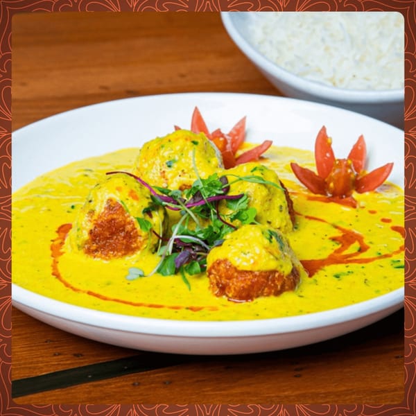 Indian malai kofta in a rich yellow curry sauce, garnished with microgreens and tomato petals.