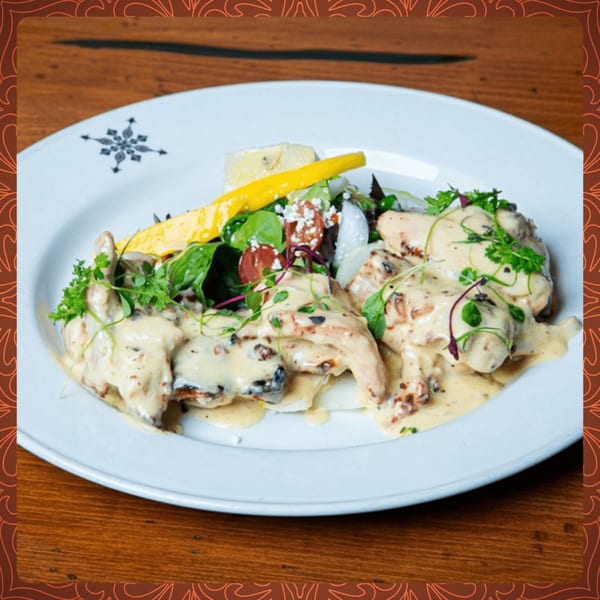 Creamy chicken dish with mushrooms and herbs, served with a side salad on a white plate.