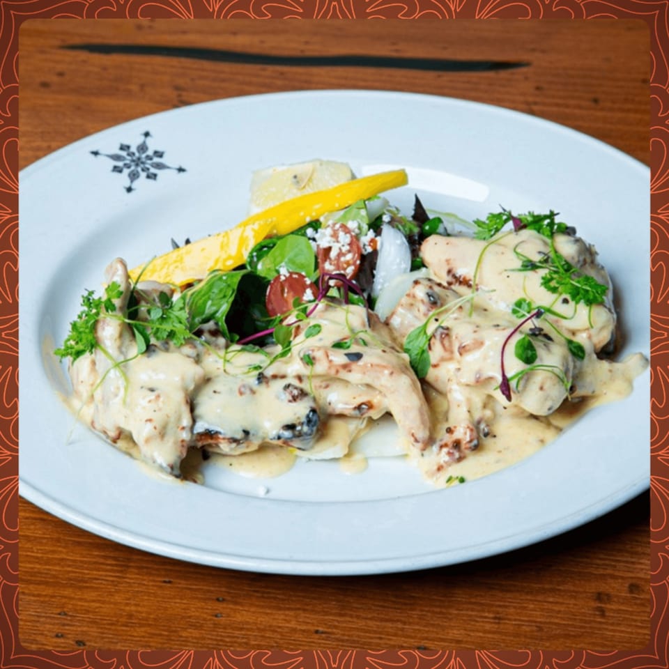 Creamy chicken dish with mushrooms and herbs, served with a side salad on a white plate.