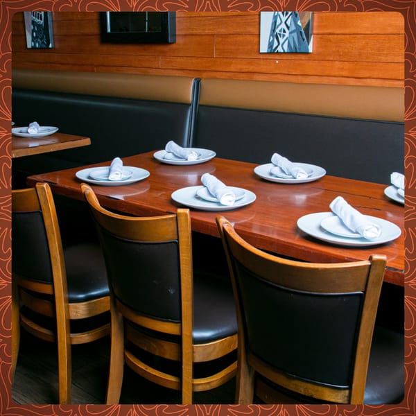 Set tables with white plates and rolled napkins in a warmly lit Indian restaurant dining room.